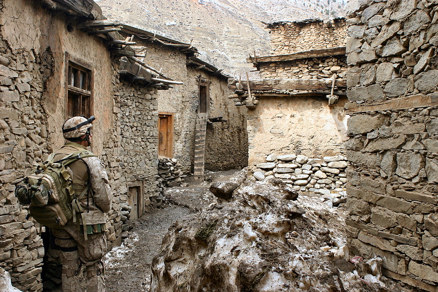 Soldier in camouflage gear walking through stone village alley