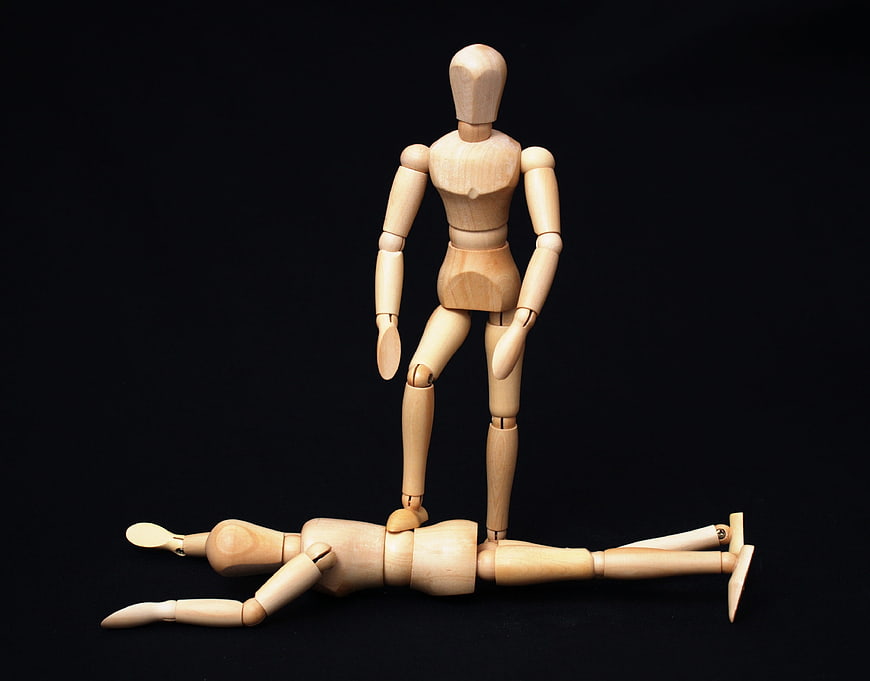 Wooden mannequins depicting dominance and defeat on black background