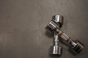 Two silver dumbbells crossed on gray foam exercise mat