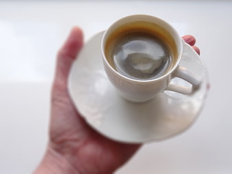 Hand holding white espresso cup on saucer