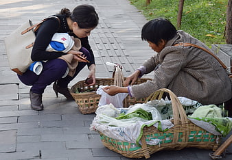 Two women buying fresh vegetables from street vendor baskets