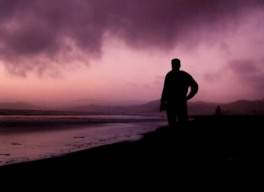 Silhouette of Man Standing on Beach at Purple Sunset