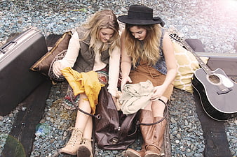 Two young women packing a bag outdoors with guitar and suitcase