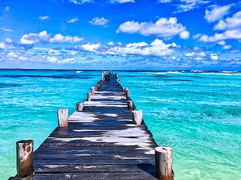 Wooden pier extending into turquoise ocean under blue sky
