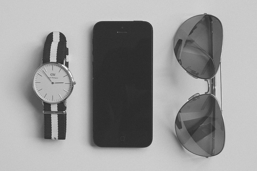 Minimalist flat lay of watch, smartphone, and sunglasses