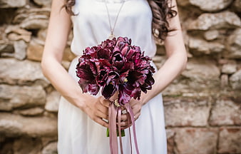 Bride holding dark purple bouquet against stone wall