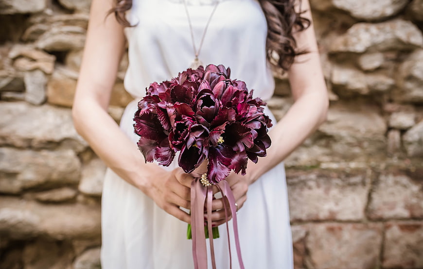 Bride holding dark purple bouquet against stone wall