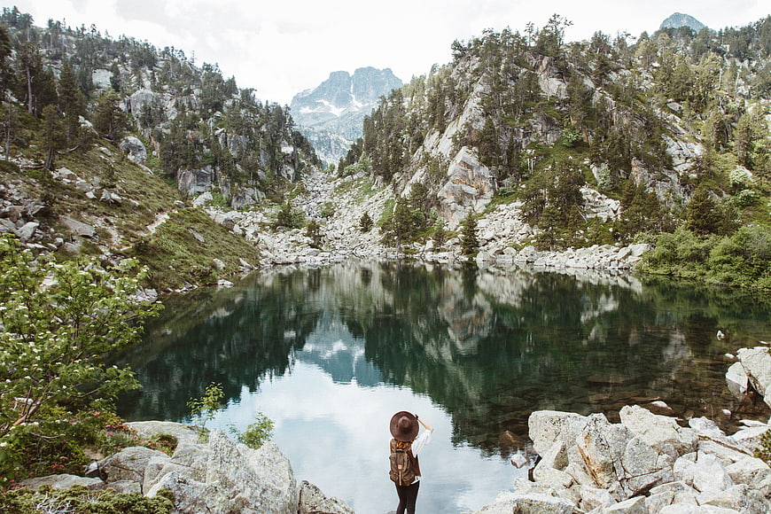 Hiker with backpack admiring mountain lake reflection