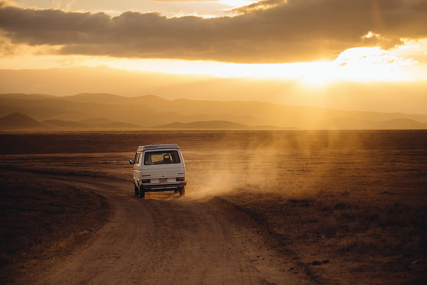 White Van Driving on Dirt Road at Sunset in Desert