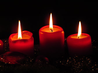 Three lit red candles on a dark background with tinsel