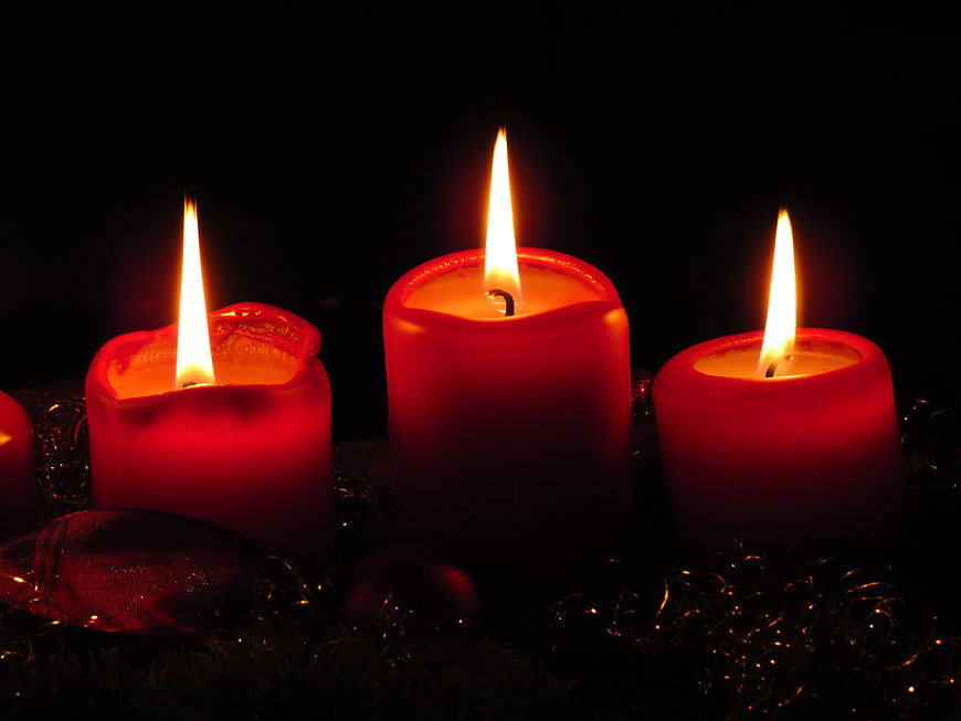 Three lit red candles on a dark background with tinsel
