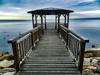 Wooden Pier with Gazebo Extending Over Calm Blue Water