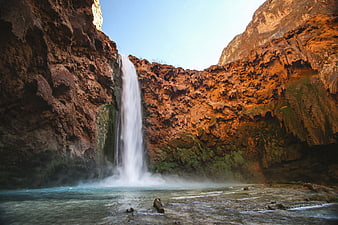 Majestic waterfall cascading into a turquoise pool in a rugged canyon