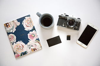 Flat lay of vintage camera, floral journal, coffee, and smartphone