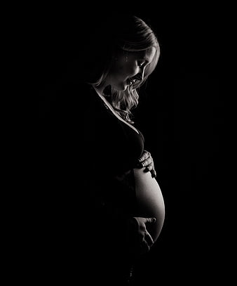Dramatic black and white silhouette of pregnant woman holding belly