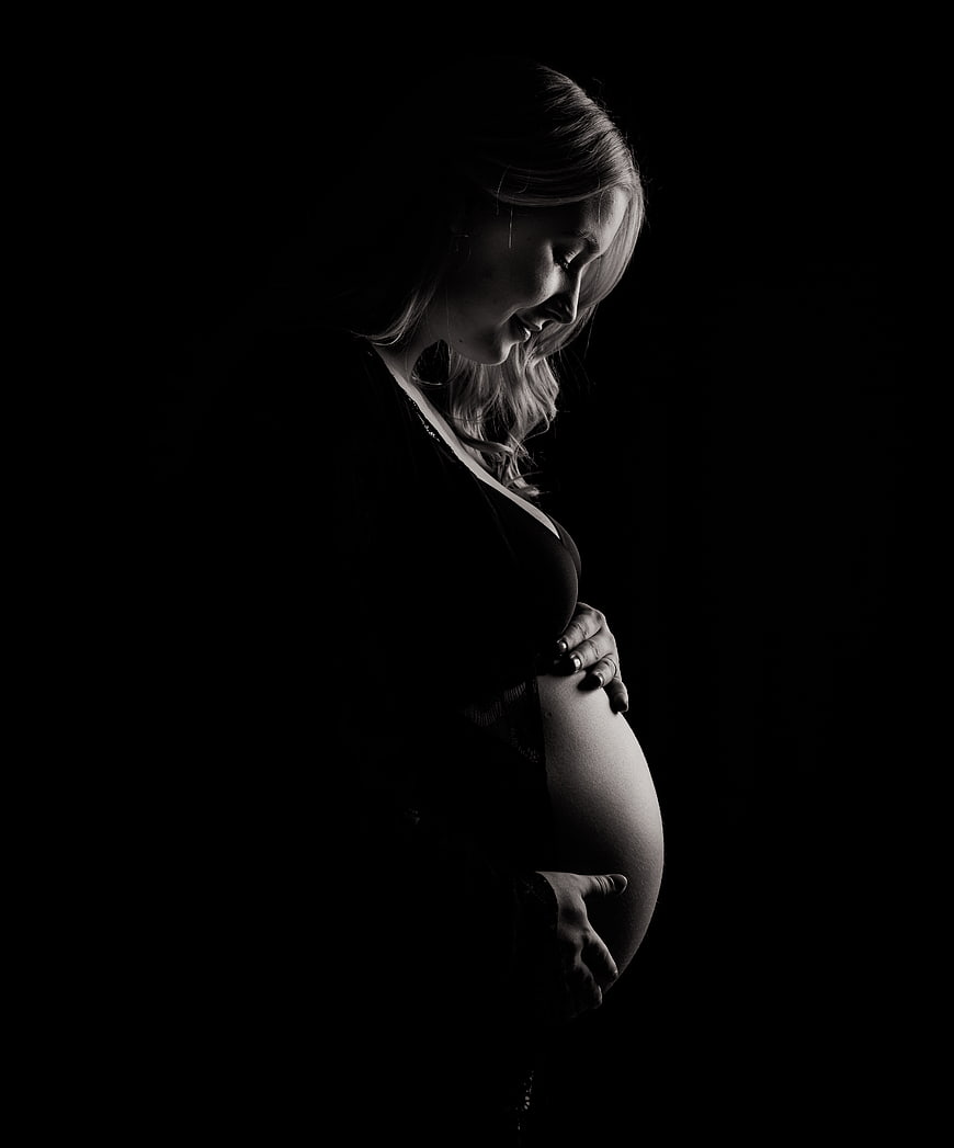 Dramatic black and white silhouette of pregnant woman holding belly