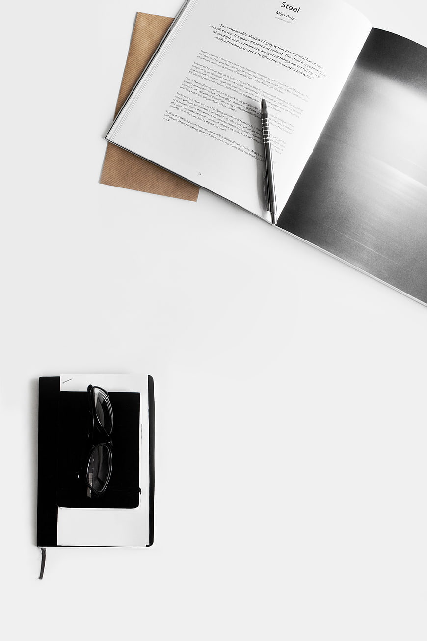 Minimalist flat lay of open magazine, notebook, and glasses on white
