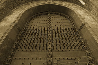 Sepia-toned ancient spiked wooden gate in stone archway