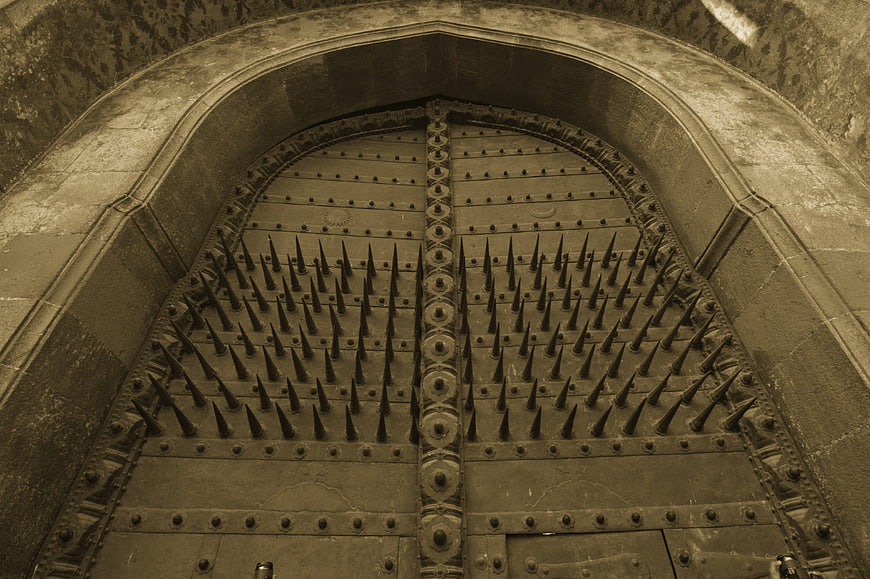 Sepia-toned ancient spiked wooden gate in stone archway