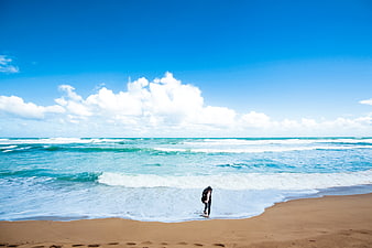 Lone Surfer Walking on Sandy Beach with Blue Sky