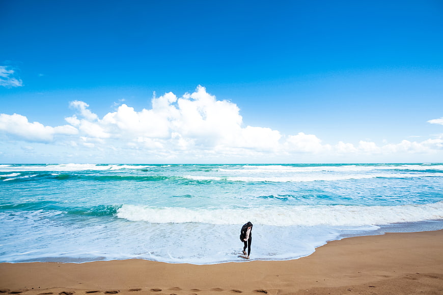 Lone Surfer Walking on Sandy Beach with Blue Sky