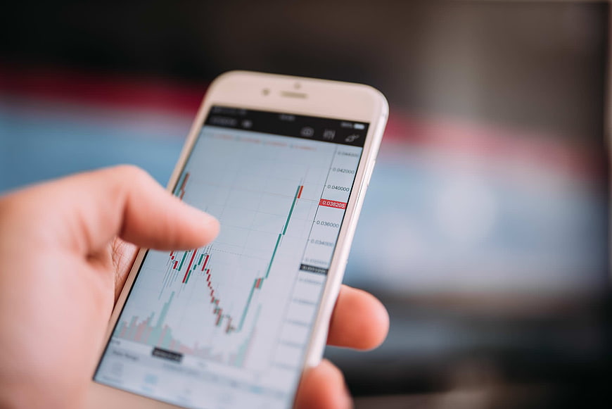 Hand holding smartphone with cryptocurrency trading chart