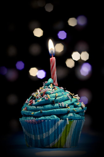 Blue frosted cupcake with lit candle and colorful bokeh background