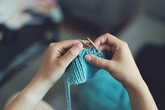 Close-up of hands knitting with blue yarn and wooden needles