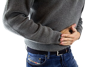 Man holding stomach in pain wearing grey sweater and jeans