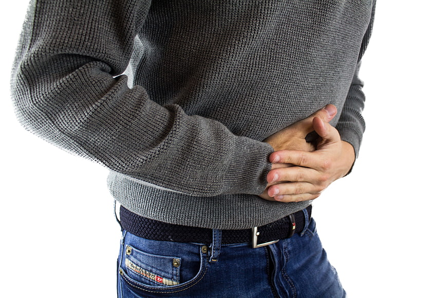 Man holding stomach in pain wearing grey sweater and jeans