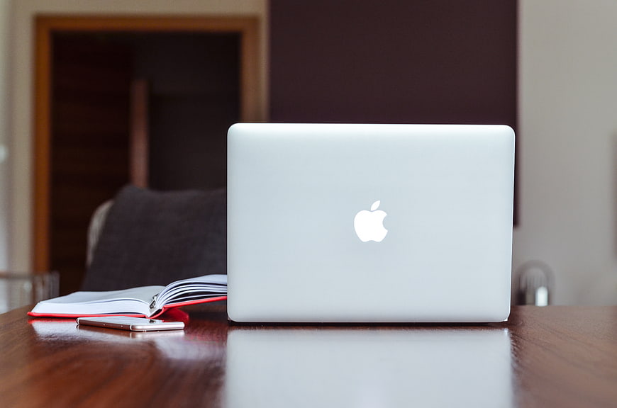 Closed MacBook on Wooden Desk with Notebook and Smartphone