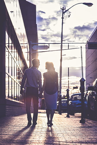 Couple holding hands walking down city street at sunset