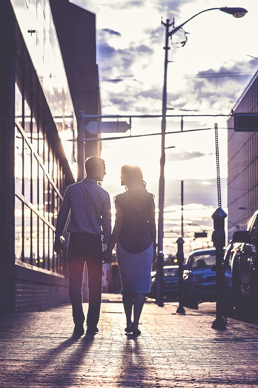 Couple holding hands walking down city street at sunset