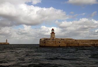 Historic stone lighthouse on a breakwater under cloudy sky