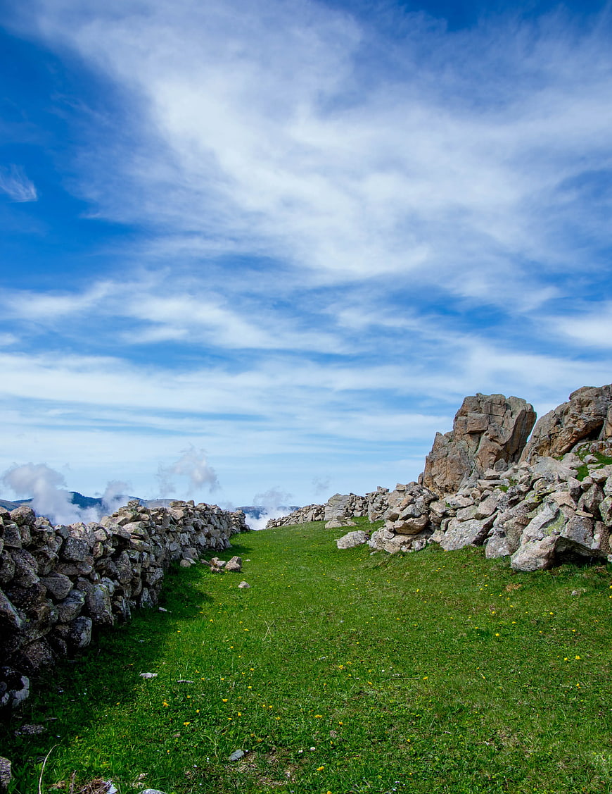 Grassy Mountain Path Between Stone Walls Under Blue Sky