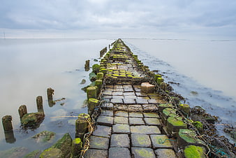 Mossy stone pier extending into calm misty sea under overcast sky