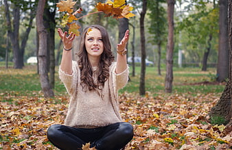 Young woman sitting in autumn park throwing maple leaves