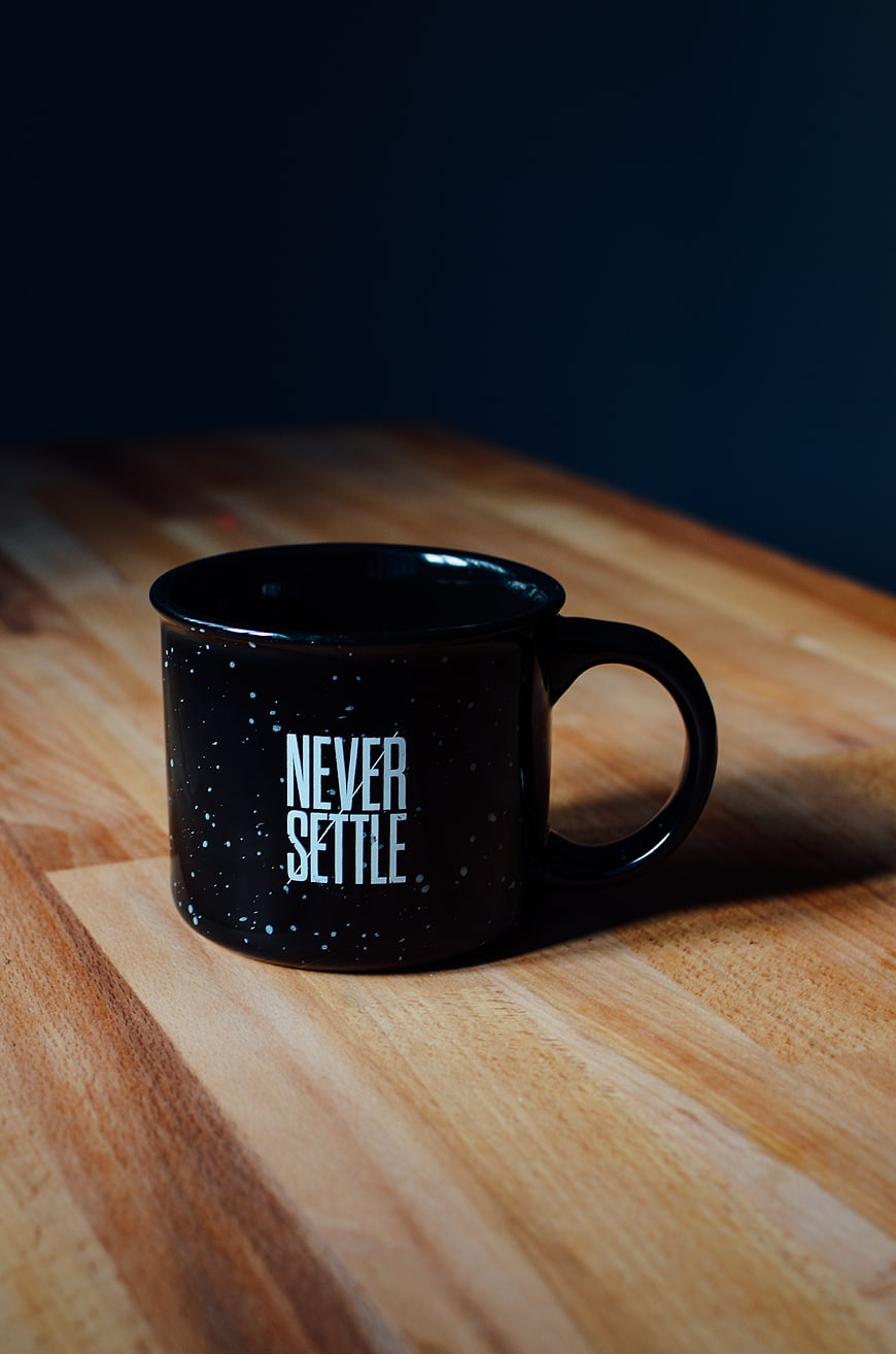 Black enamel mug with Never Settle quote on wooden table