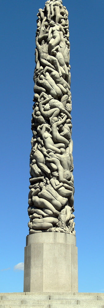 Monumental stone sculpture of intertwined human figures against blue sky