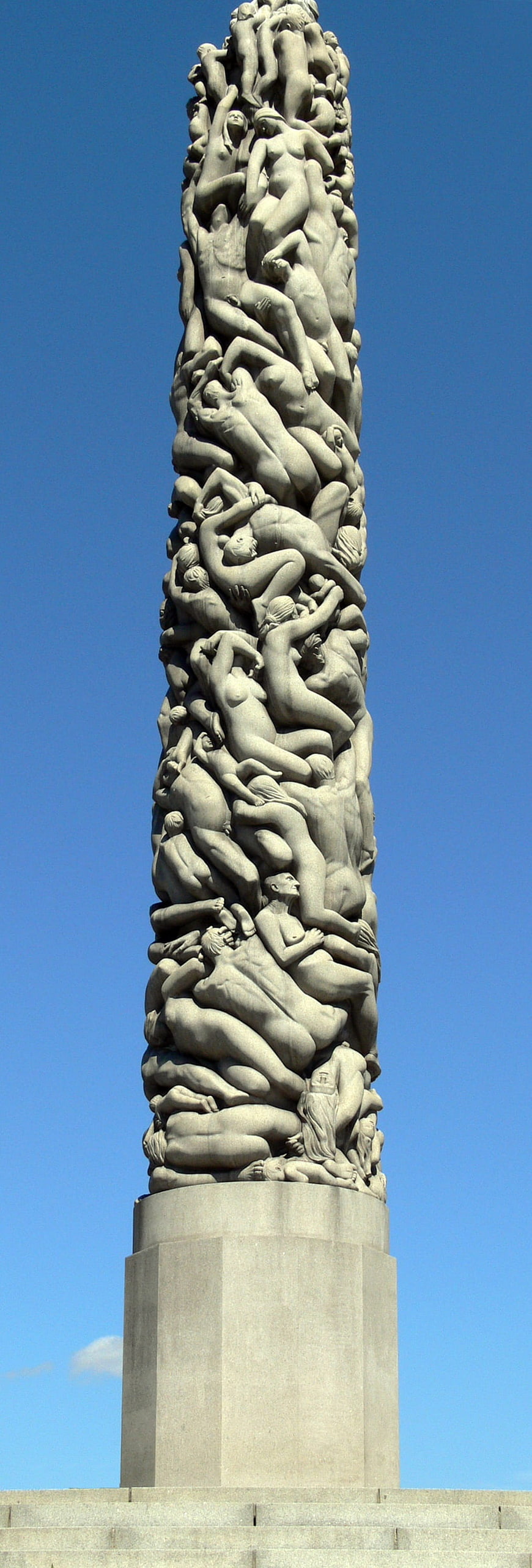 Monumental stone sculpture of intertwined human figures against blue sky