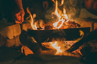 Close-up of hand tending a crackling campfire at night