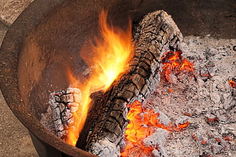 Burning wood logs and glowing embers in a metal fire pit