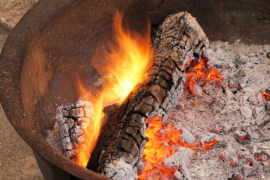 Burning wood logs and glowing embers in a metal fire pit