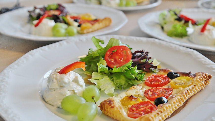 Gourmet tart with salad, cheese, and grapes on white plate