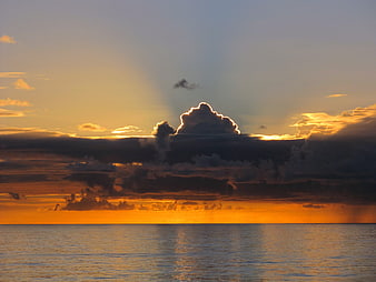 Dramatic sunset over ocean with golden light rays through clouds