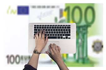 Hands typing on laptop with blurred 100 euro banknotes in background