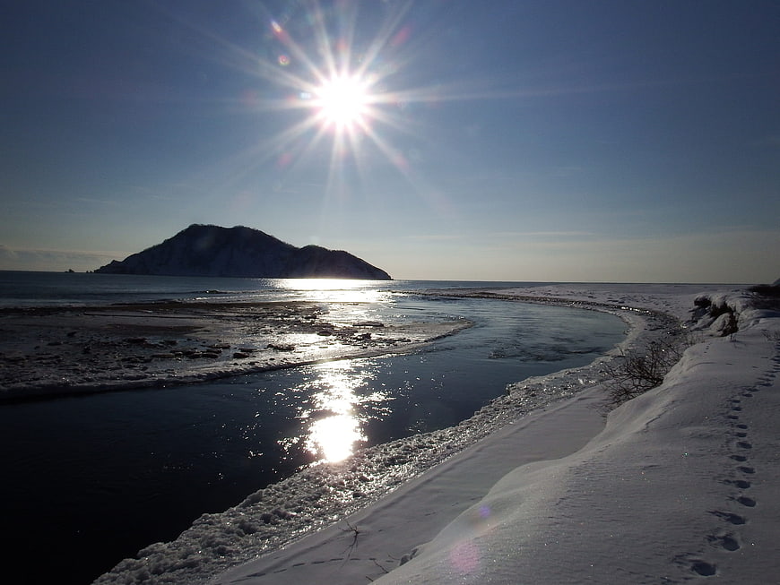Winter coastal landscape with sunburst over snowy river and island