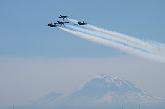 Four jets flying in formation with smoke trails over a mountain