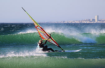 Windsurfer riding a wave with city skyline in background