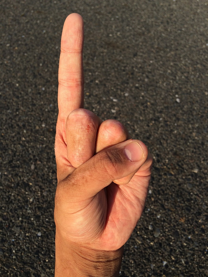Close-up of hand making number one finger gesture on asphalt